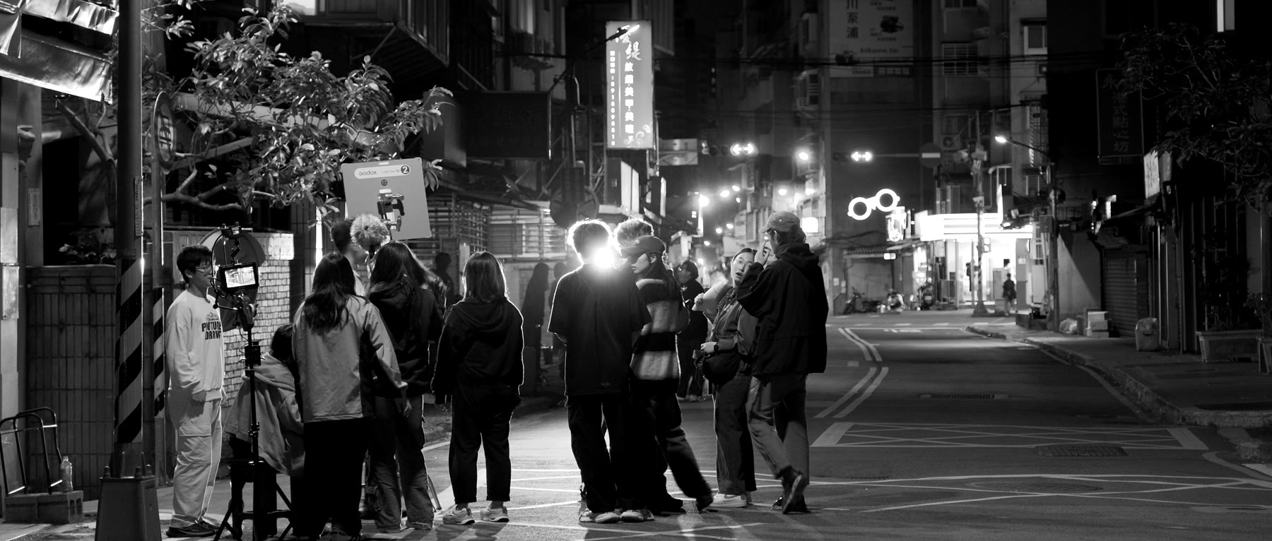 夜間外景現場:工作人員聚在監看器旁,身後是亮著招牌的街道